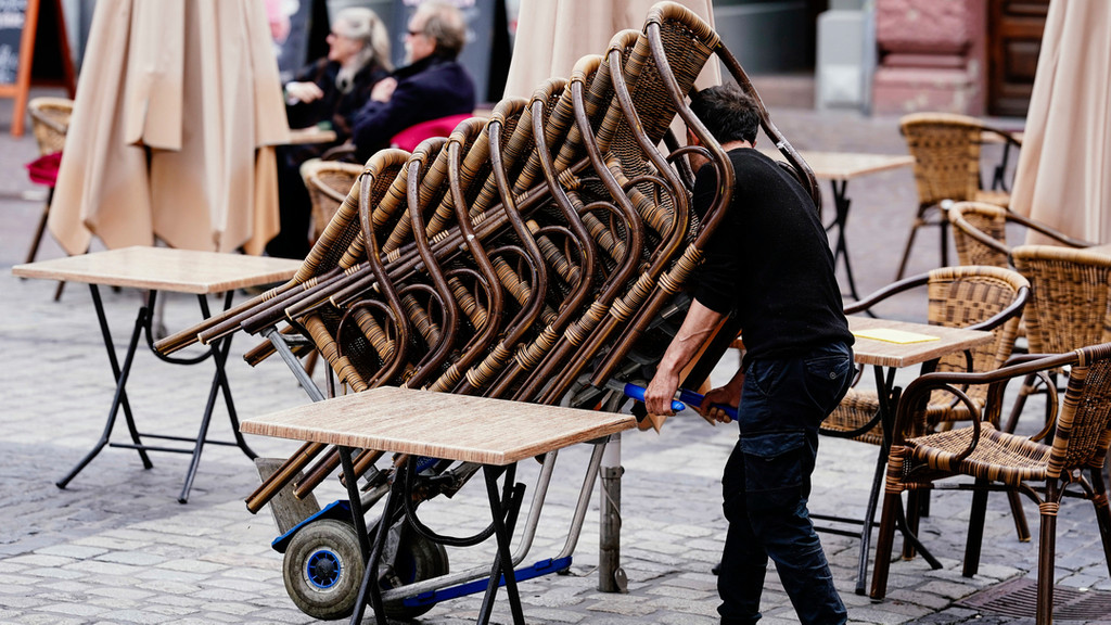 Der Mitarbeiter einer Gaststätte rollt einen Stapel Stühlee auf den Marktplatz