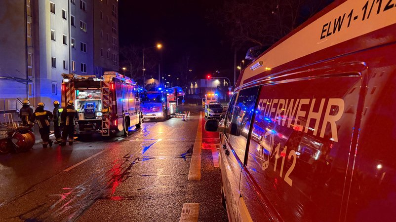 Einsatzfahrzeuge der Feuerwehr stehen auf einer regennassen Straße vor einem Mehrfamilienhaus. Auf der Straße sind mehrere Einsatzkräfte zu sehen. | Bild: NEWS5 / Sven Grundmann Einsatzfahrzeuge der Feuerwehr stehen auf einer regennassen Straße vor einem Mehrfamilienhaus. Auf der Straße sind mehrere Einsatzkräfte zu sehen.