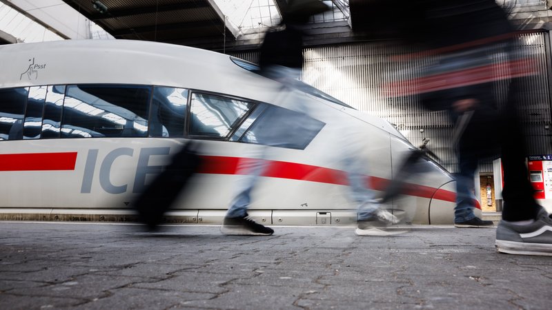 Reisende gehen an einem Bahnsteig an einem ICE der Deutschen Bahn am Hauptbahnhof von München vorüber.