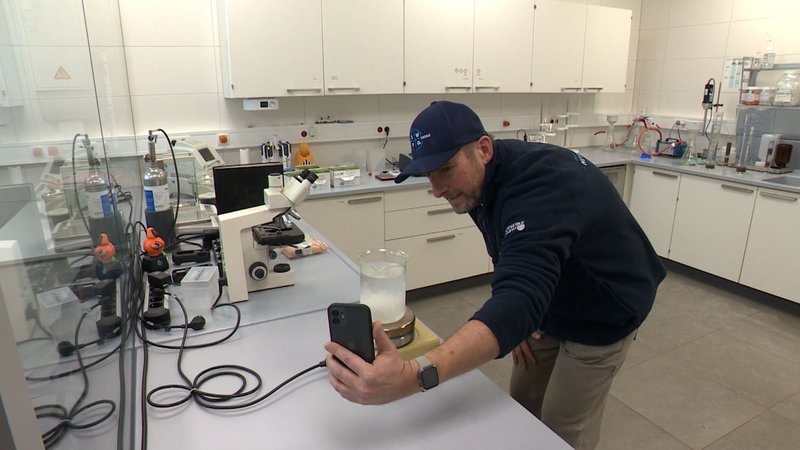 Gernot Reichel steht mit einem Smartphone in einem Labor der Kläranlage Forchheim.