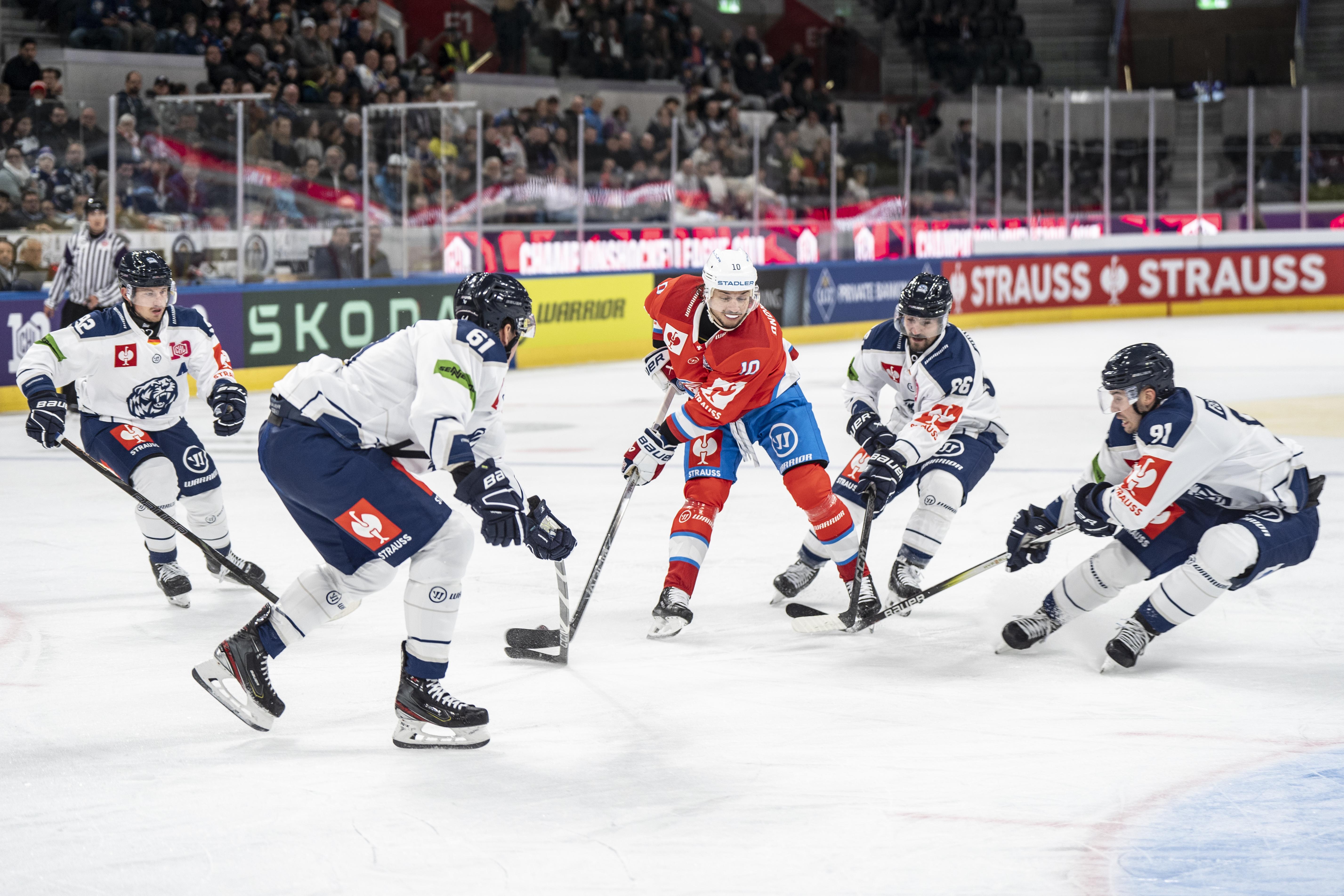 Vier Eishockeyspieler kämpfen auf dem Eis um den Puck. 
