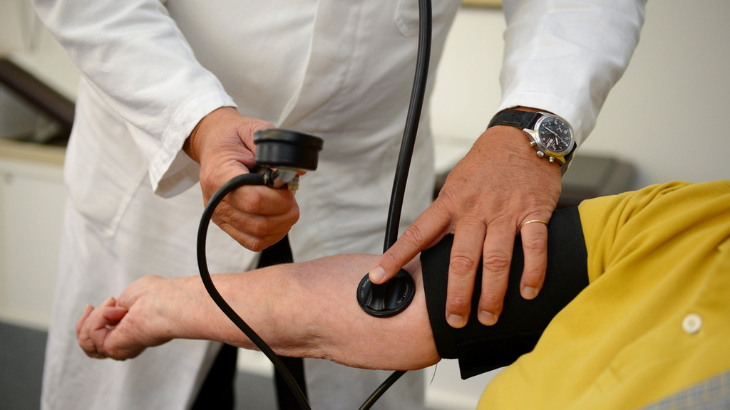Ein Hausarzt misst in seiner Praxis einer Patientin den Blutdruck.