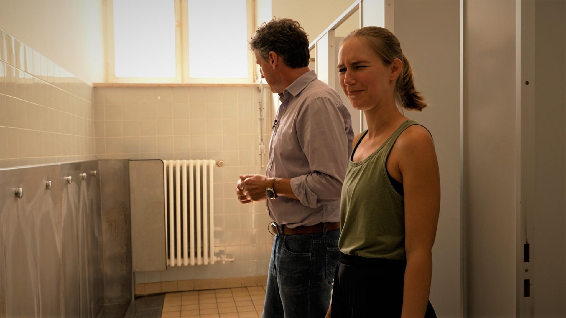 Schulleiter Michael Böck steht zusammen mit Elternbeirätin Anja Waninger in der Schul-Toilette. Es stinkt nach Urin, Waninger schaut angeekelt in die Kamera.