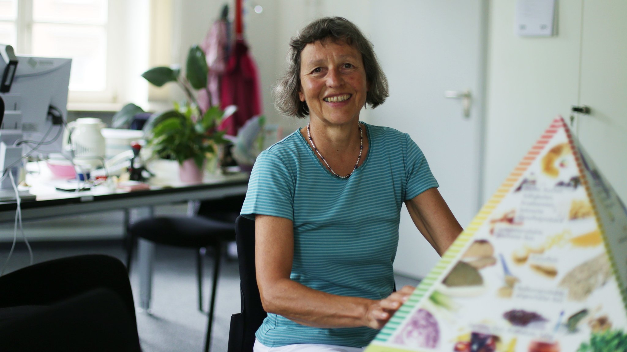 Dorothee Volkert sitzt in ihrem Büro vor einer Ernährungspyramiede.