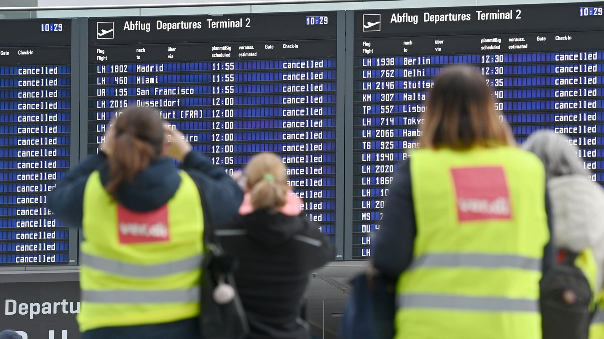 Streikende am Münchner Flughafen stehen vor den Übersichtstafeln, die die ausgefallenen Flüge anzeigen.