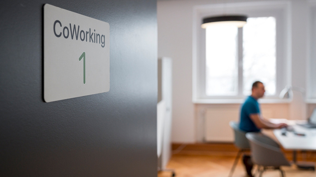 Auf einer Tür zu einem Büro steht "Coworking 1", drinnen sitzt ein Mann an einem Schreibtisch und arbeitet an einem Computer.