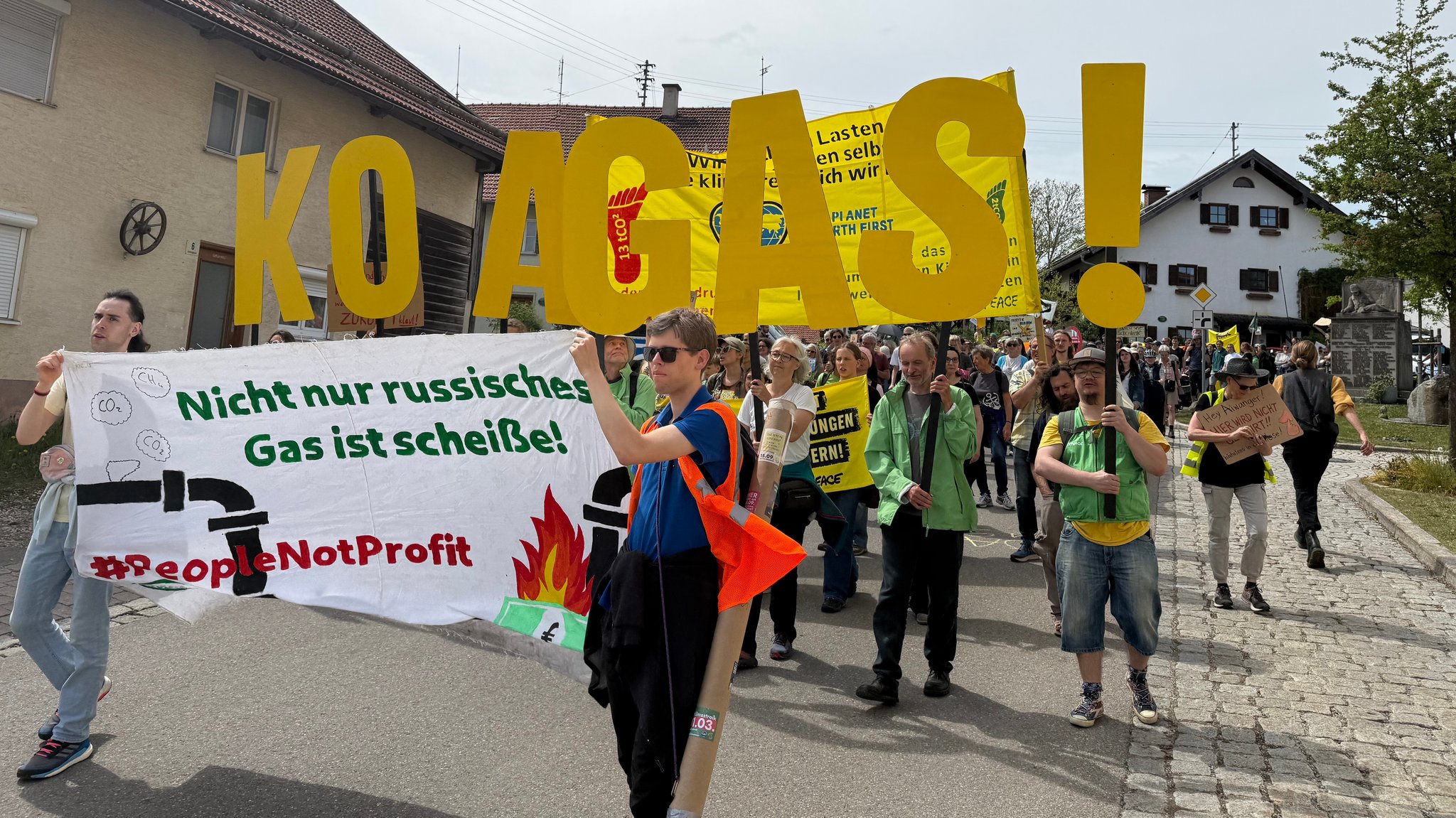 Demonstrierende ziehen durchs Dorf und halten Schilder hoch, auf denen "Koa Gas!" und "Nicht nur russisches Gas ist scheiße!" steht.