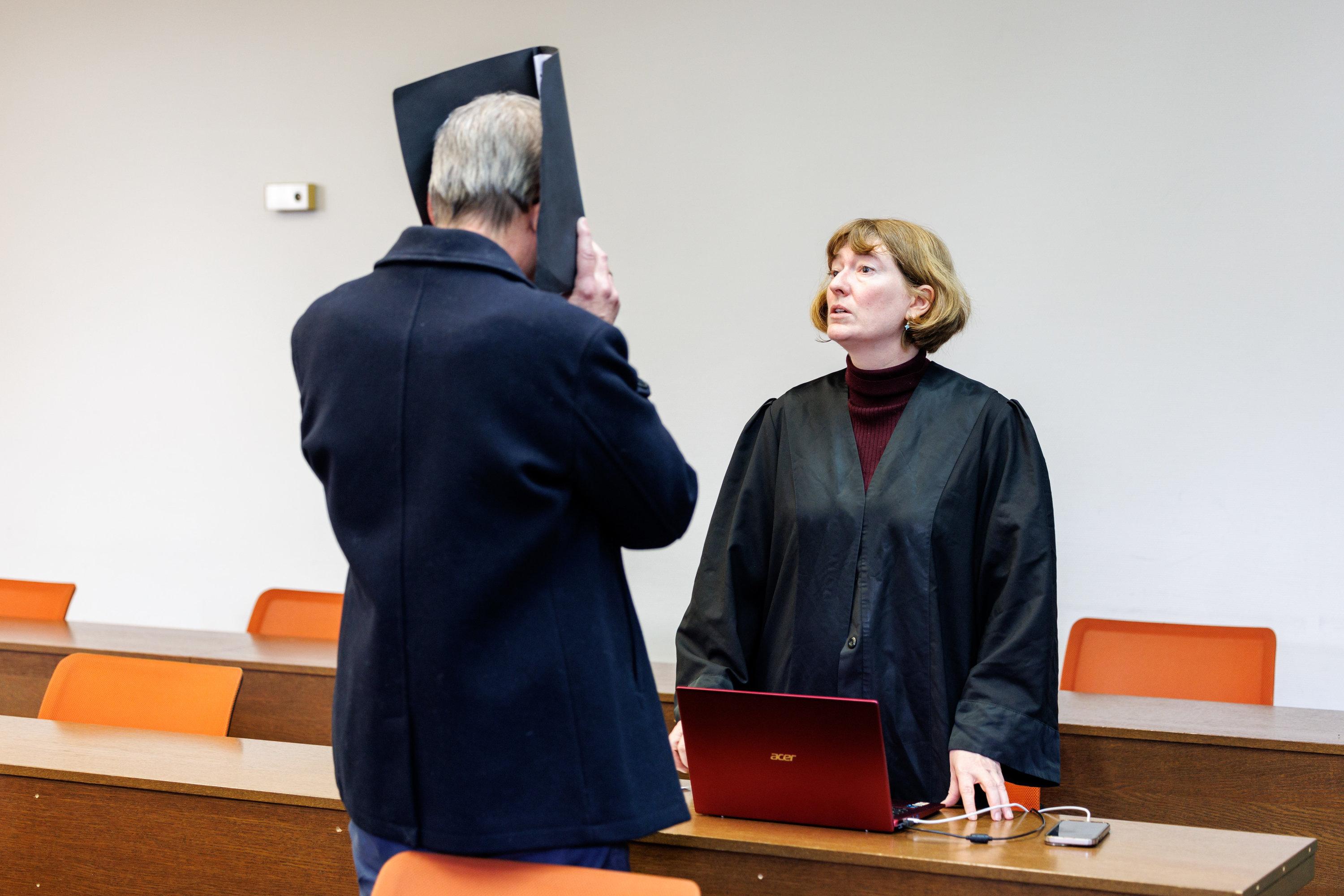 ARCHIV - 07.01.2025, Bayern, München: Der Angeklagte (l), ein wegen sexuellen Übergriffs und sexueller Nötigung angeklagter Arzt, steht vor Prozessbeginn in einem Gerichtssaal vom Landgericht München I, hält sich eine Mappe vor sein Gesicht und spricht mit seiner Rechtsanwältin Julia Weinmann. Der Angeklagte soll mehrere betäubte Patientinnen während Darmspiegelungen vergewaltigt haben. (zu dpa: «Arzt wegen Vergewaltigung von Patientinnen verurteilt - Haft») Foto: Matthias Balk/dpa +++ dpa-Bildfunk +++