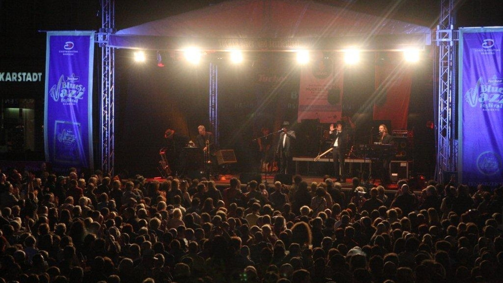 Beim Blues- und Jazzfestival in Bamberg an einem Augustabend im Jahr 2018 stehen Musiker auf einer Bühne und geben ein Konzert. Viele Zuschauer stehen davor und hören zu. 