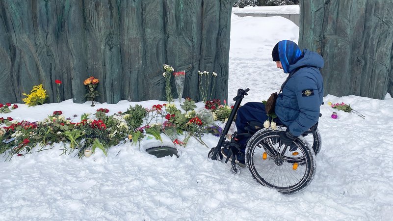 Ein Rollstuhlfahrer legt Blumen nieder | Bild: Aleksandr Chernykh/Picture Alliance Ein Rollstuhlfahrer legt Blumen nieder