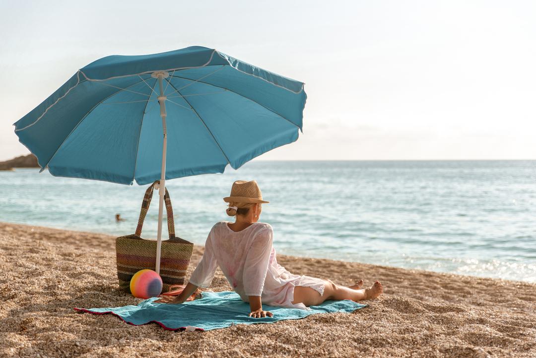 Eine Frau sitzt unter einem Sonnenschirm am Strand.