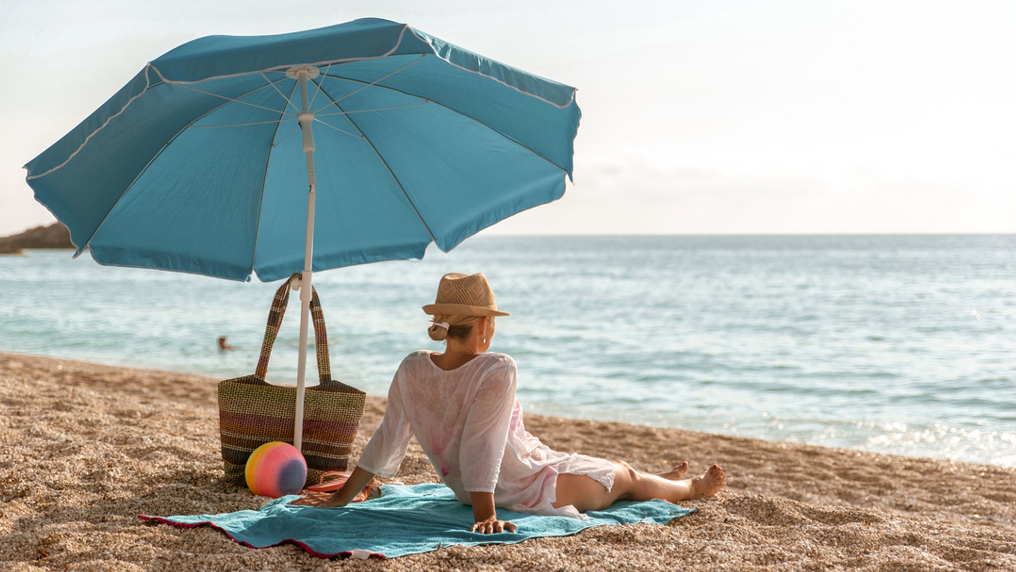 Eine Frau sitzt unter einem Sonnenschirm am Strand.