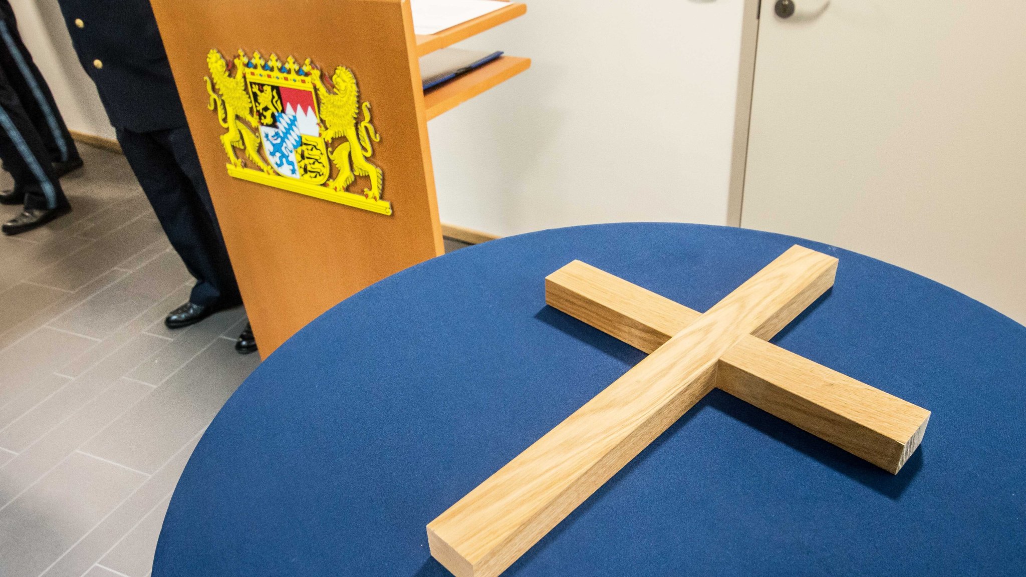 Ein großes Holzkreuz liegt auf einem Tisch. Daneben ist das bayerische Wappen zu sehen.