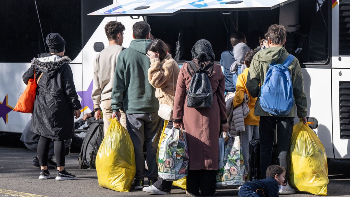 Flüchtlinge mit Tüten und anderem Gepäck vor einem Bus 