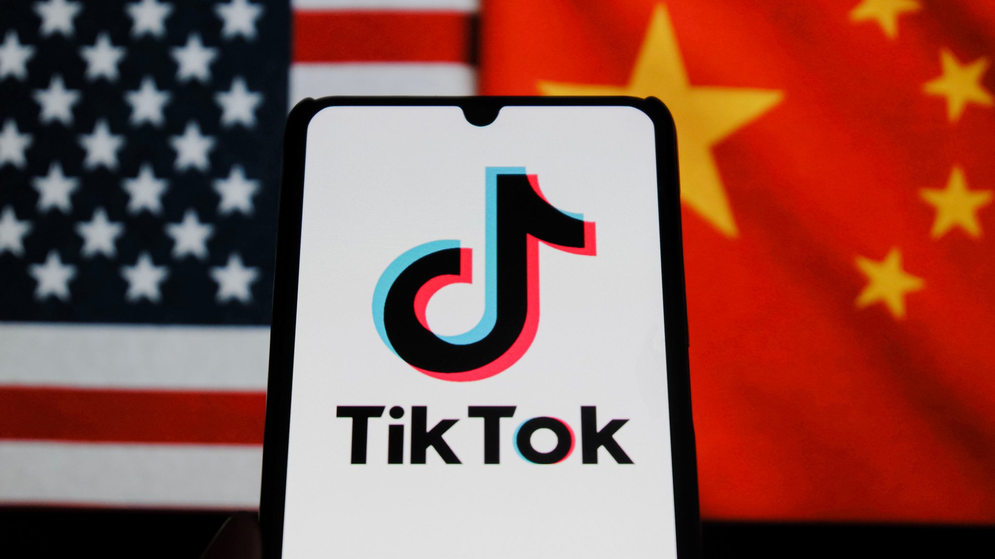 Illustration: Smartphone mit TikTok-Logo vor den Flaggen der USA und China