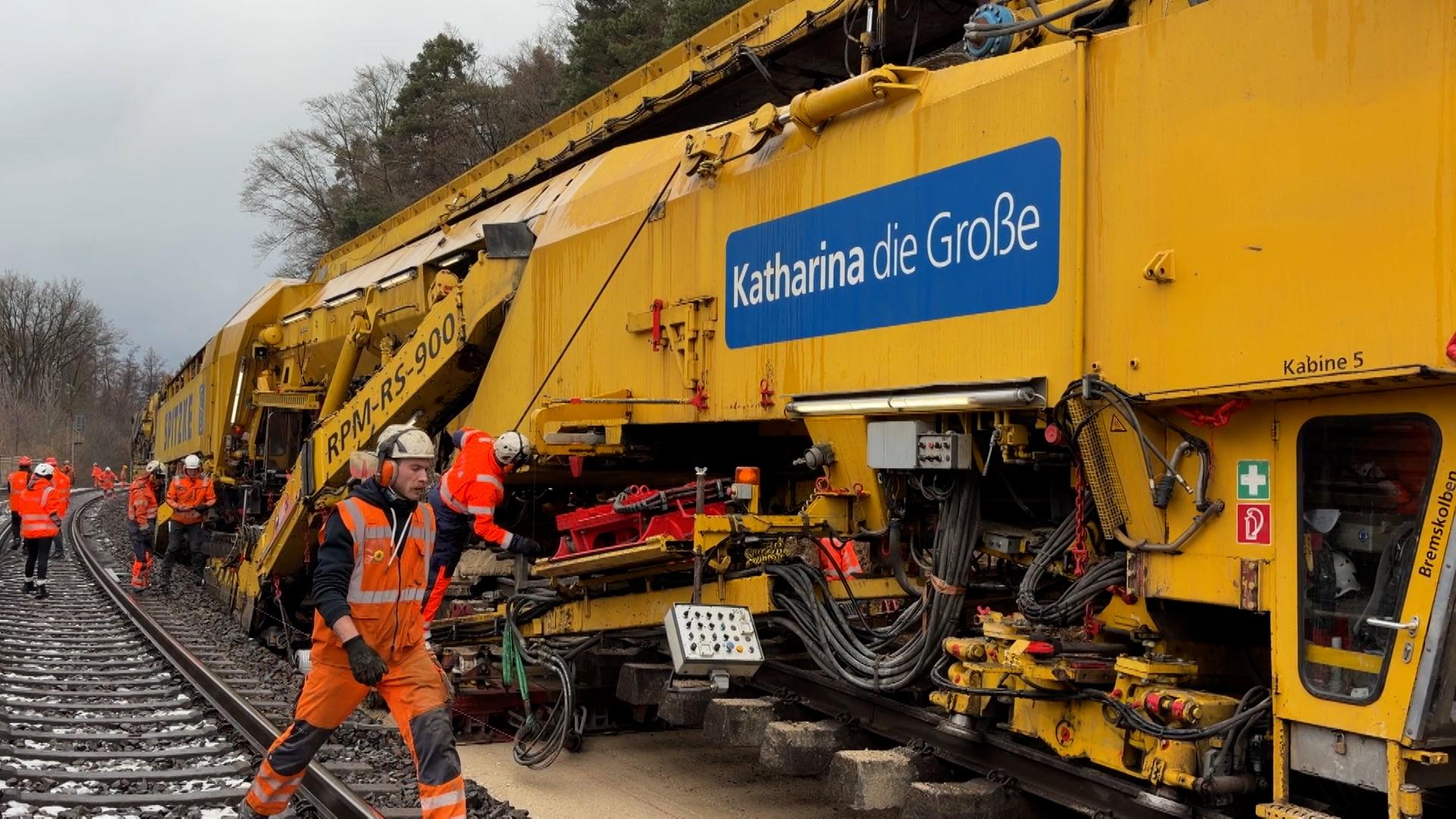 Arbeiter in orangenen Westen an der gelben Gleisbaumaschine "Katharina die Große".