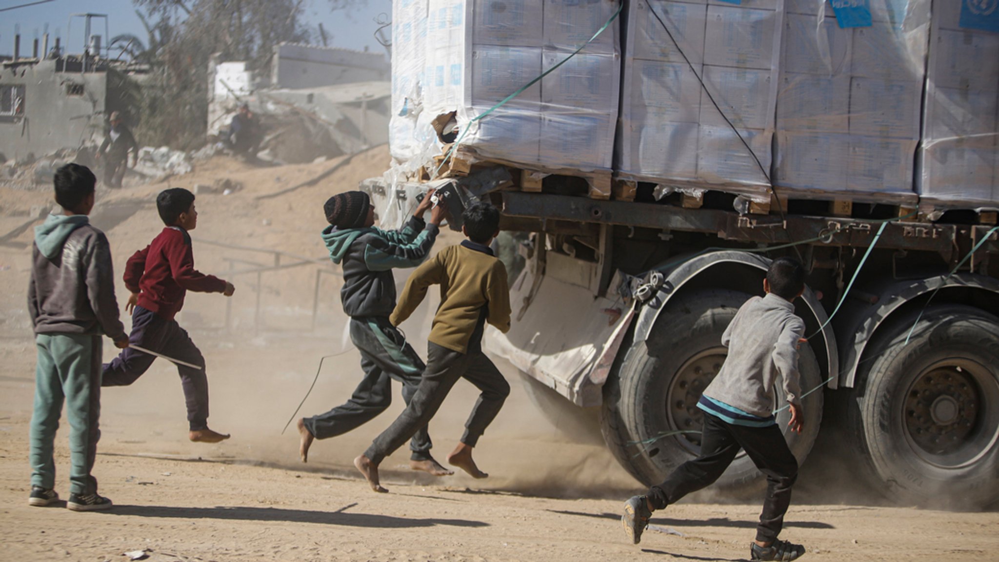 21.01.2025, Palästinensische Gebiete, Rafah: Palästinenser rennen einem Lastwagen mit humanitären Hilfsgütern nach, der über den Kerem-Shalom-Übergang von Ägypten in den Gazastreifen eingefahren ist.