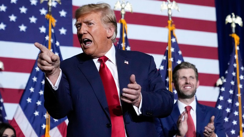 USA, Des Moines: Donald Trump, ehemaliger Präsident der USA, zeigt neben seinem Sohn Eric bei einer Caucus-Party auf die Menge.