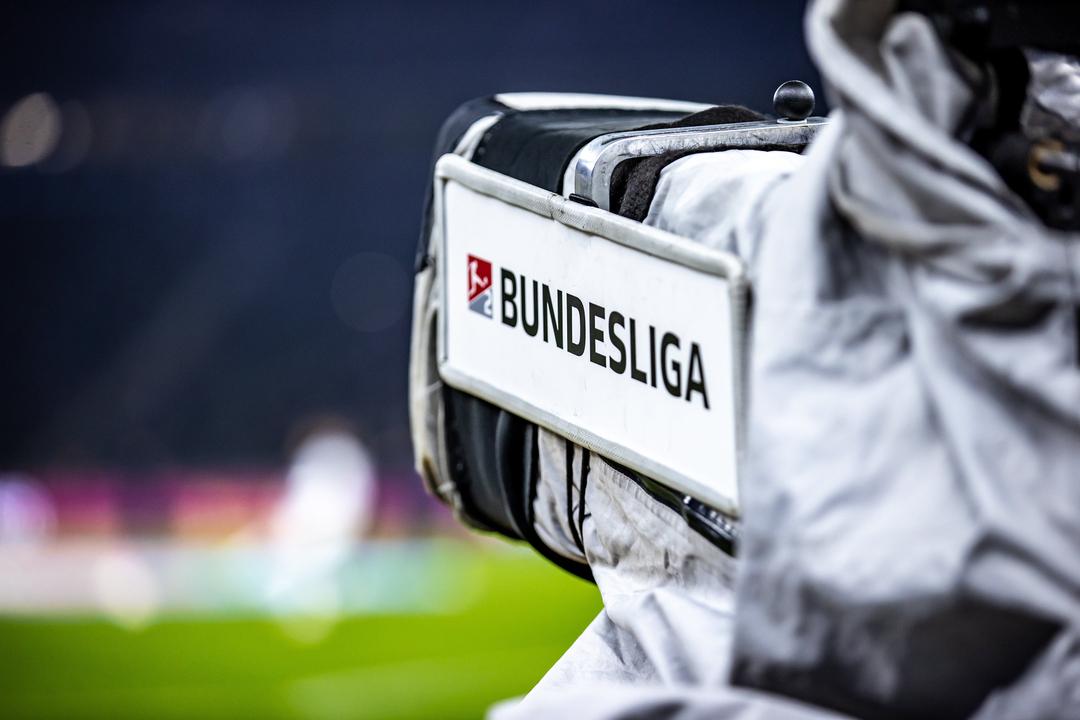Eine Kamera mit Schriftzug "Bundesliga" ist auf einen Fußball-Platz gerichtet.