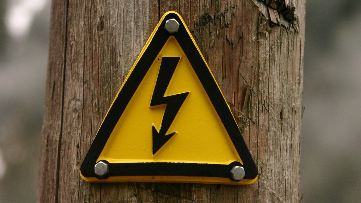 Symbolbild: Gelbes Schild mit gezacktem schwarzem Pfeil "Achtung Strom". 