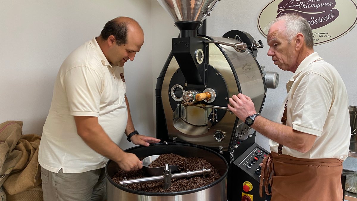Der alte und der neue Besitzer der Rösterei stehen vor der Rösttrommel und kontrollieren die braunen Kaffeebohnen