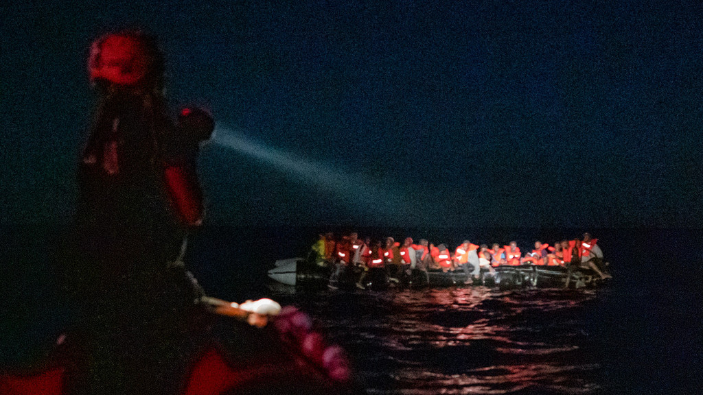 Der Lichtkegel einer Taschenlampe leuchtet auf flüchtende Menschen in einem Schlauchboot.