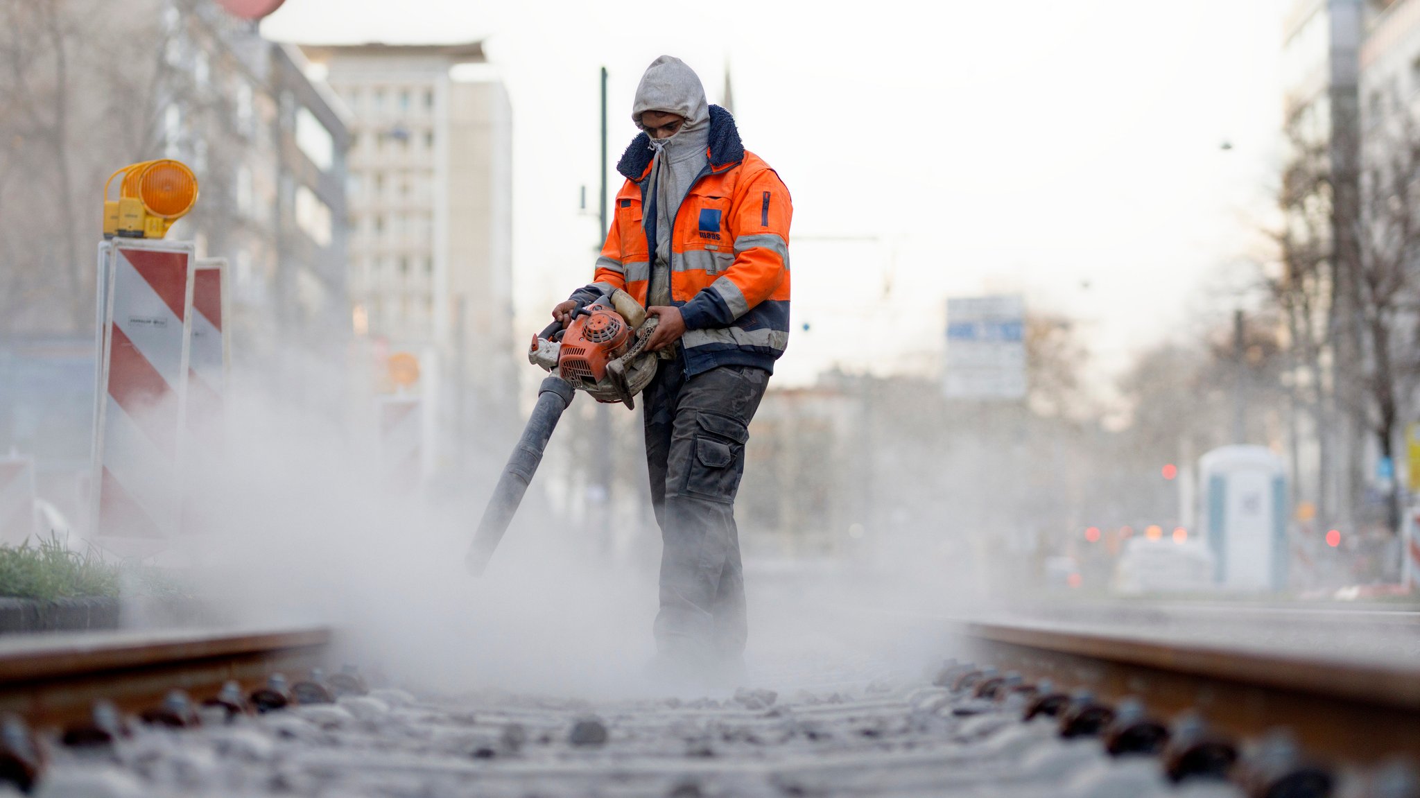 Symbolbild: Ein Bauarbeiter bläst Betonstaub von Bahnschienen. 