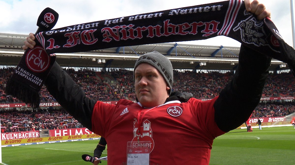 Rene Funken steht vor der Nordkurve im Max-Morlock-Stadion, hält seinen Fanschal in die Höhe und sing die Vereinshymne "Die Legende lebt". 