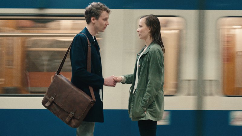Ein junger Mann und eine junge Frau geben sich unsicher die Hand vor einer U-Bahn.