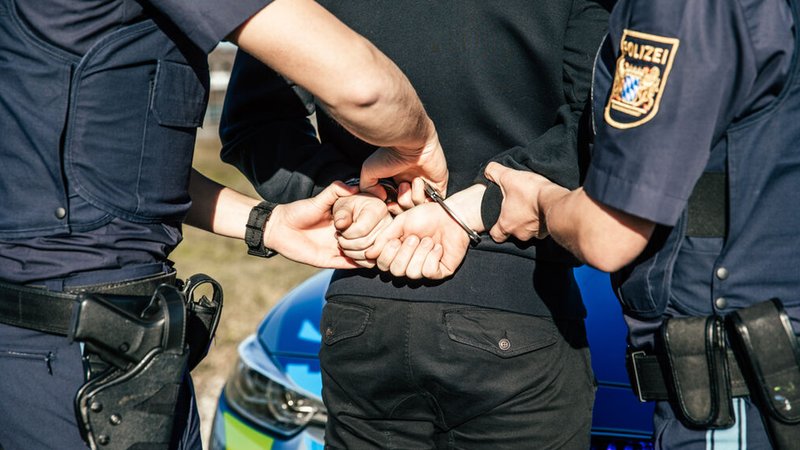 Eine Polizistin und ein Polizist legen einem jungen Mann Handschellen an.