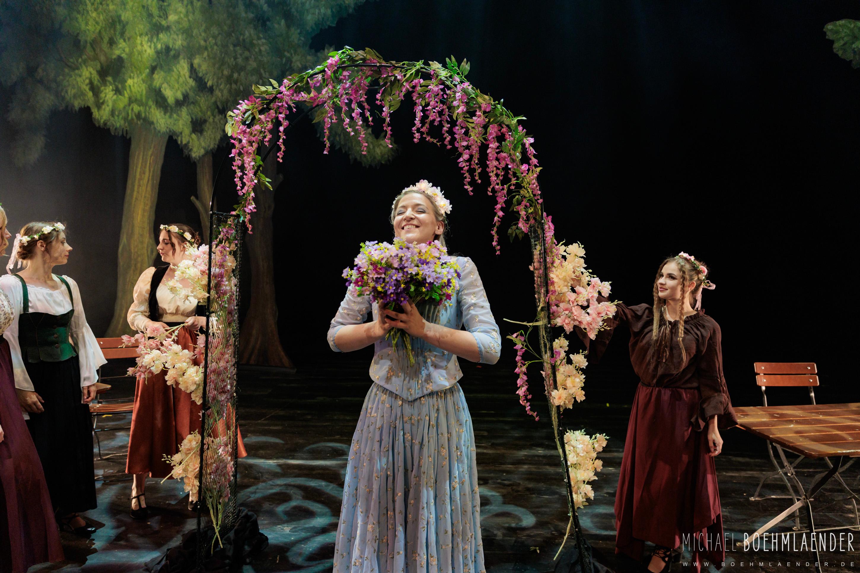 Darstellerin mit einem üppigen Blumenstrauß unter einem mit Ranken geschmückten Bogen