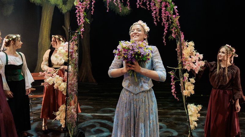 Darstellerin mit einem üppigen Blumenstrauß unter einem mit Ranken geschmückten Bogen | Bild: Michael Böhmländer/Festspielhaus Füssen Darstellerin mit einem üppigen Blumenstrauß unter einem mit Ranken geschmückten Bogen