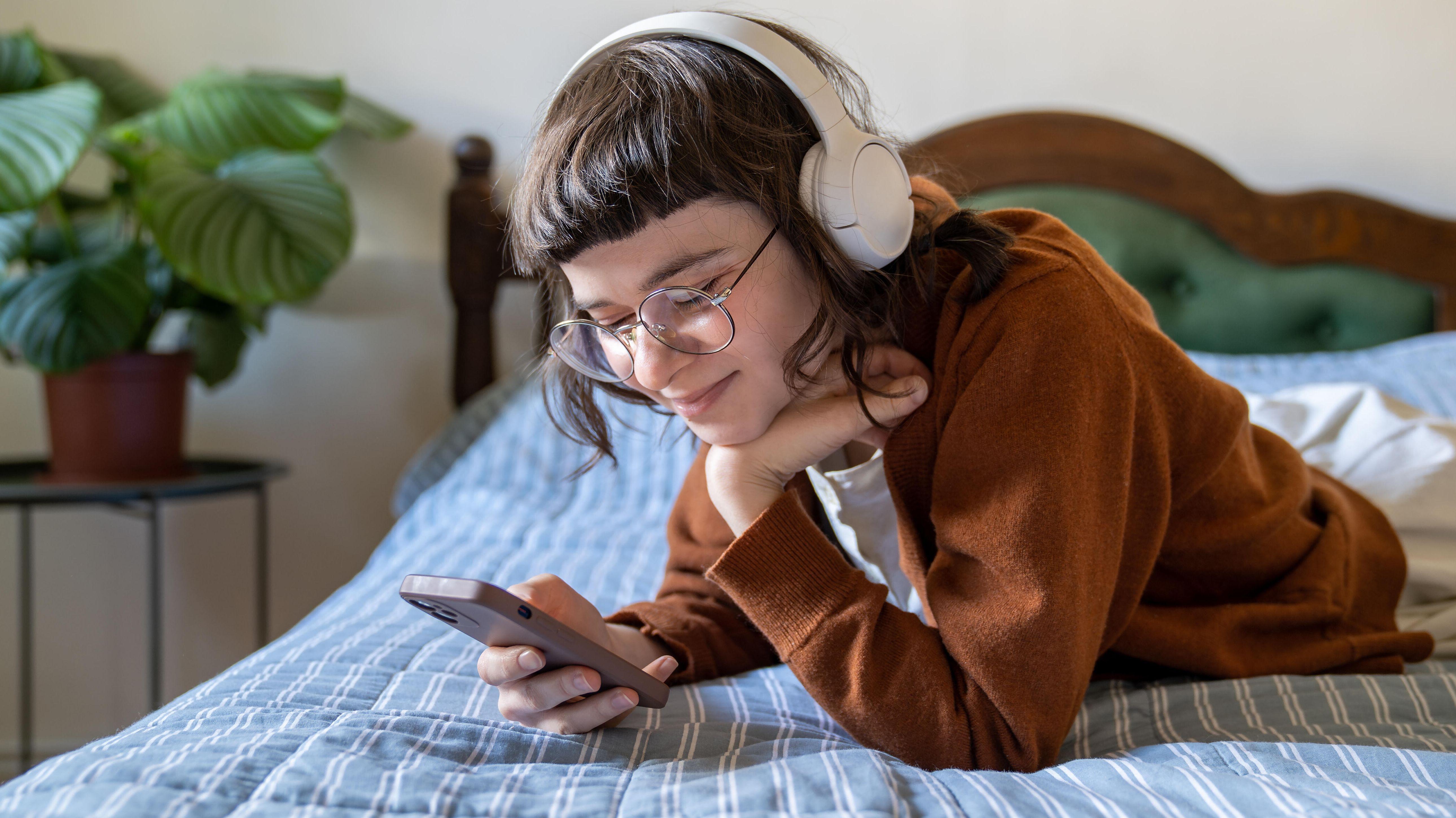 Eine junge Frau liegt auf dem Bett und schaut lächelnd in ihr Smartphone.