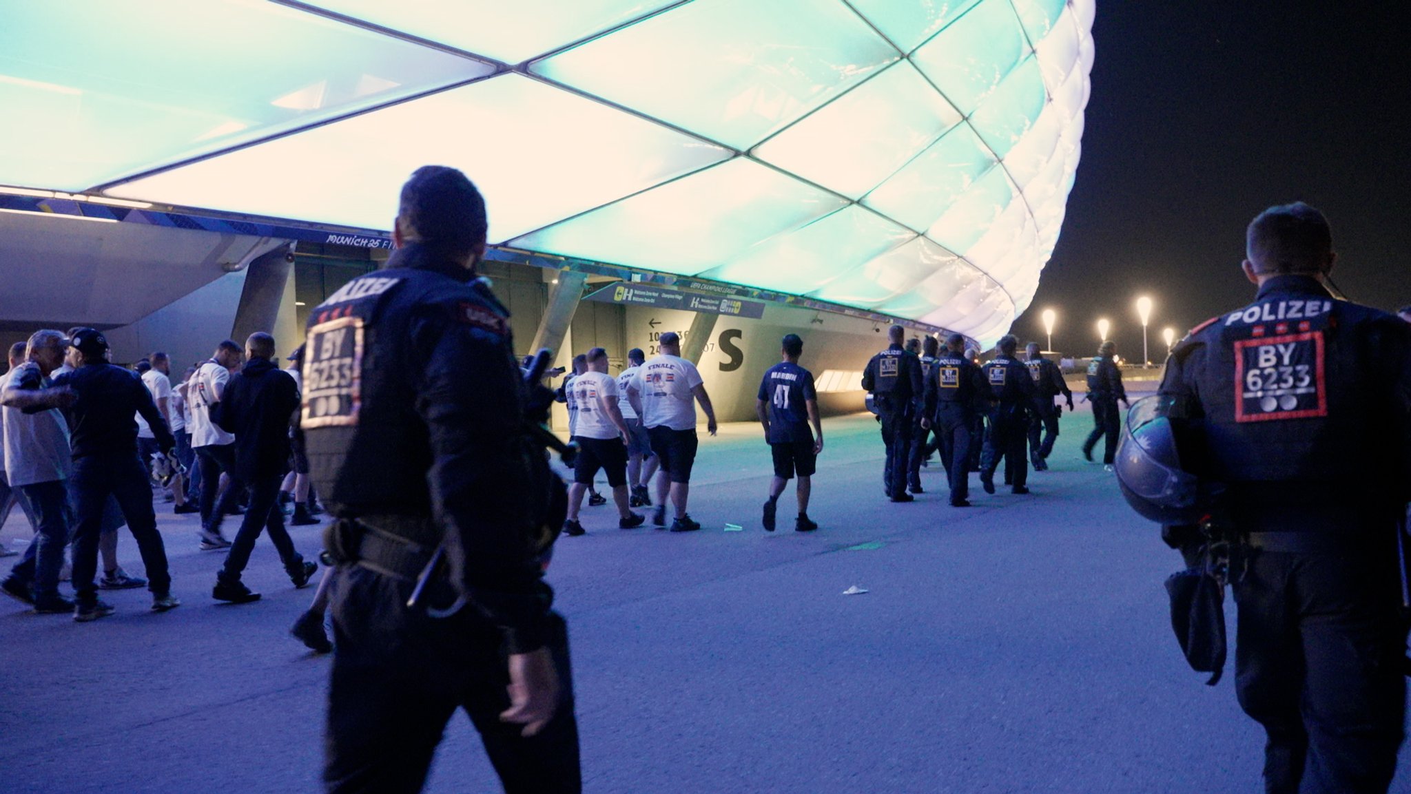Foto: Etwa 10 Polizeibeamte begleiten eine Gruppe von Fußballfans außerhalb der Münchner Fußballarena. Es ist Nacht. | Bild: BR / Moritz Steinbacher Foto: Etwa 10 Polizeibeamte begleiten eine Gruppe von Fußballfans außerhalb der Münchner Fußballarena. Es ist Nacht.