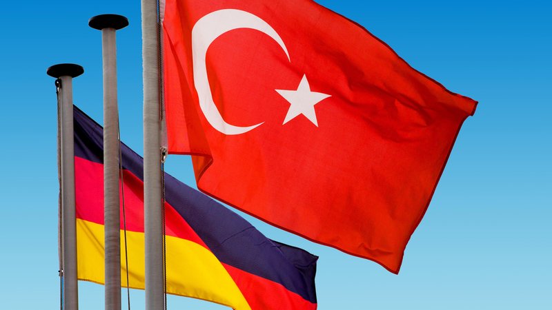 Türkische und deutsche Nationalflaggen wehen vor blauem Himmel.