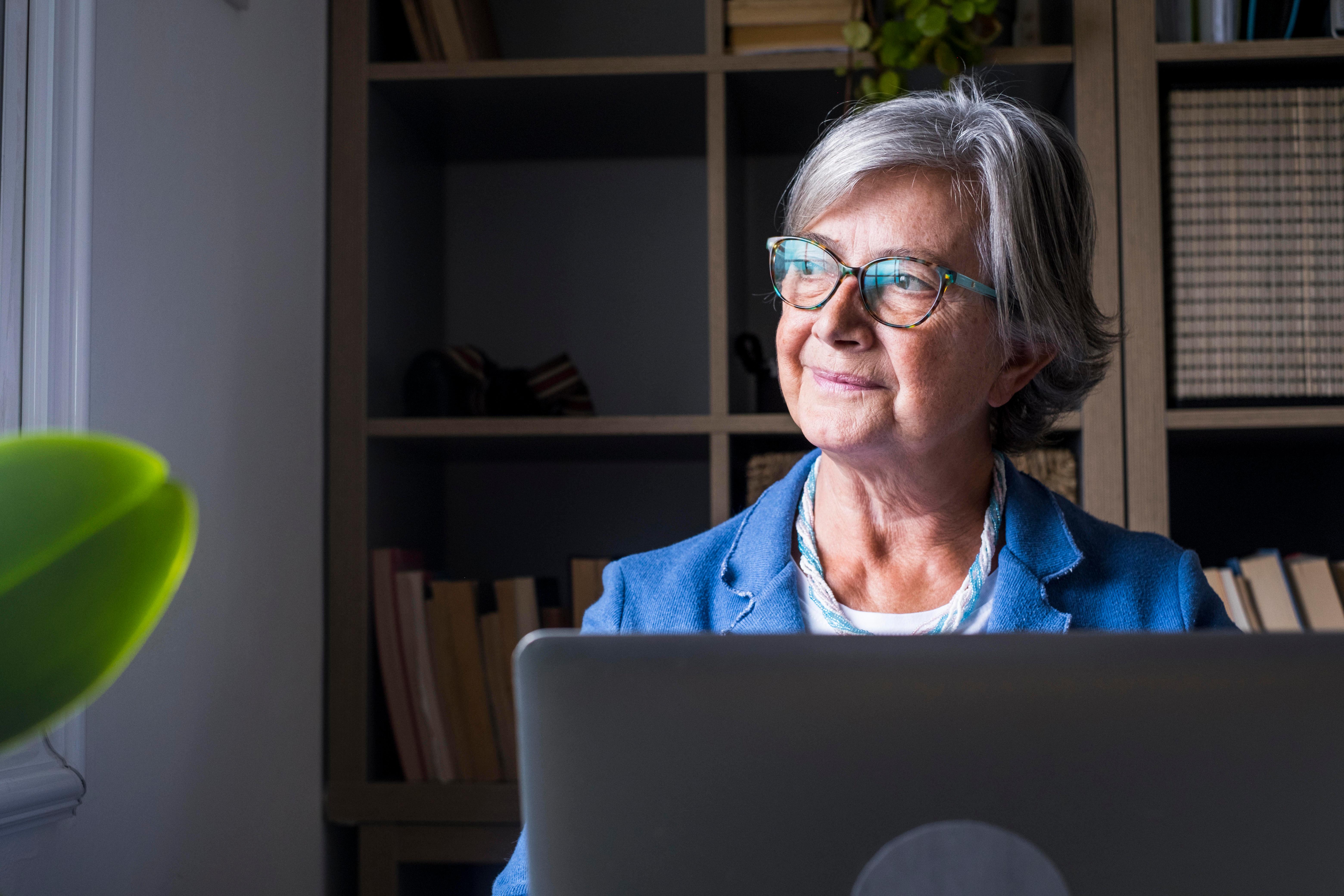 Weiter arbeiten, trotz Rentenbezügen. Wenn die Steuerlast nicht zu hoch ist, kann sich das lohnen. Eine Frau sitzt am Laptop und schaut nachdenklich aus dem Fenster (Symbolbild)