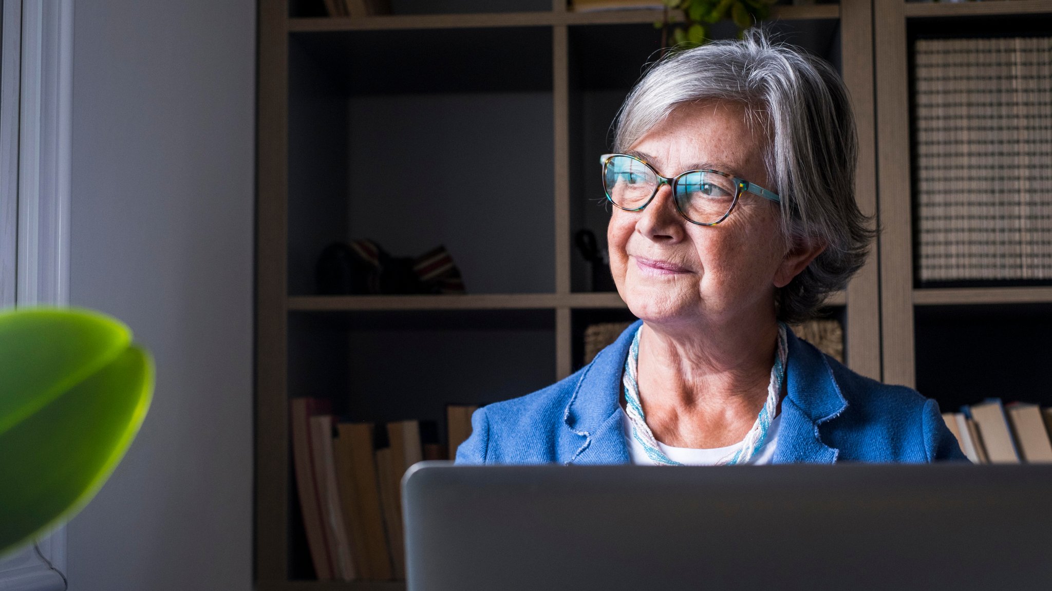 Weiter arbeiten, trotz Rentenbezügen. Wenn die Steuerlast nicht zu hoch ist, kann sich das lohnen. Eine Frau sitzt am Laptop und schaut nachdenklich aus dem Fenster (Symbolbild)