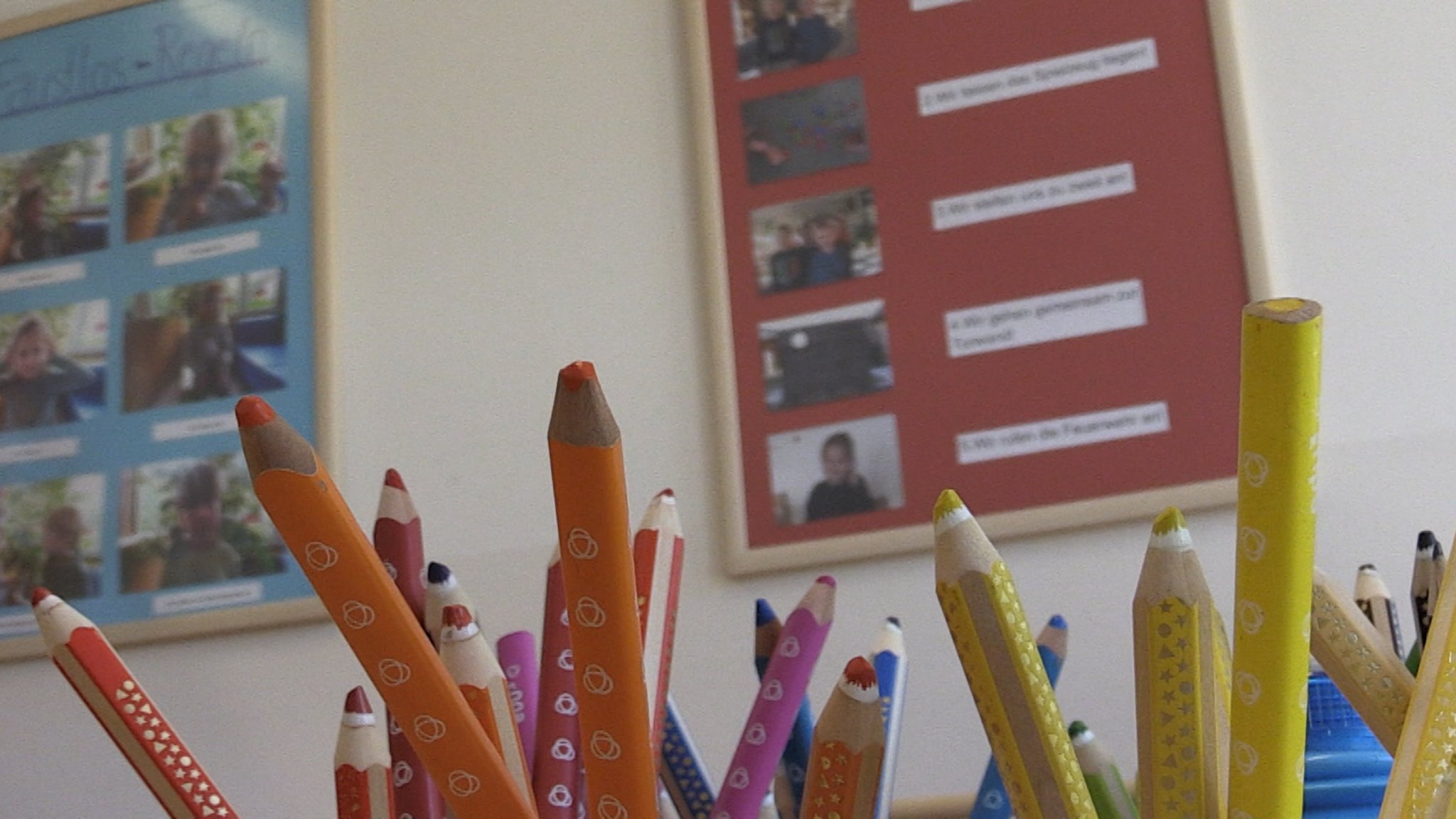 Mehrere Buntstifte vor einer Wand mit Kinderfotos - aus der Kia "Kleine Welt" in Ingolstadt.