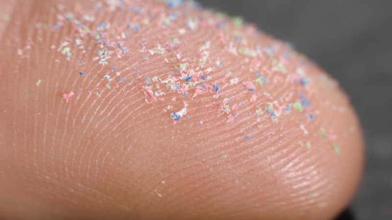 Winzige, farbige Mikroplastikteilchen auf einer Fingerkuppe