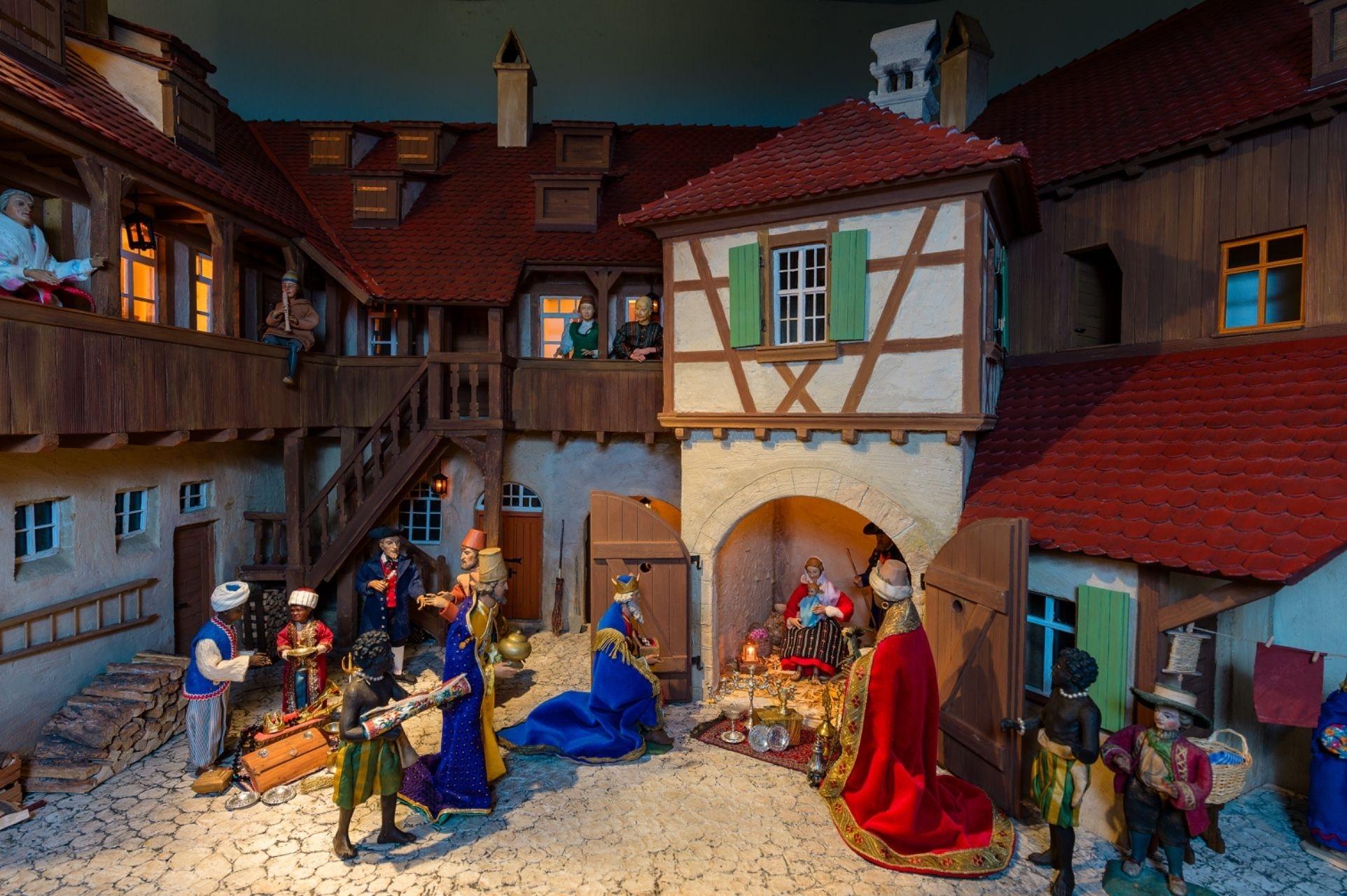 In einer krippe sind bunt gekleidete Figuren vor einem Fachwerkhaus aufgestellt, darunter die Heiligen drei Könige. 