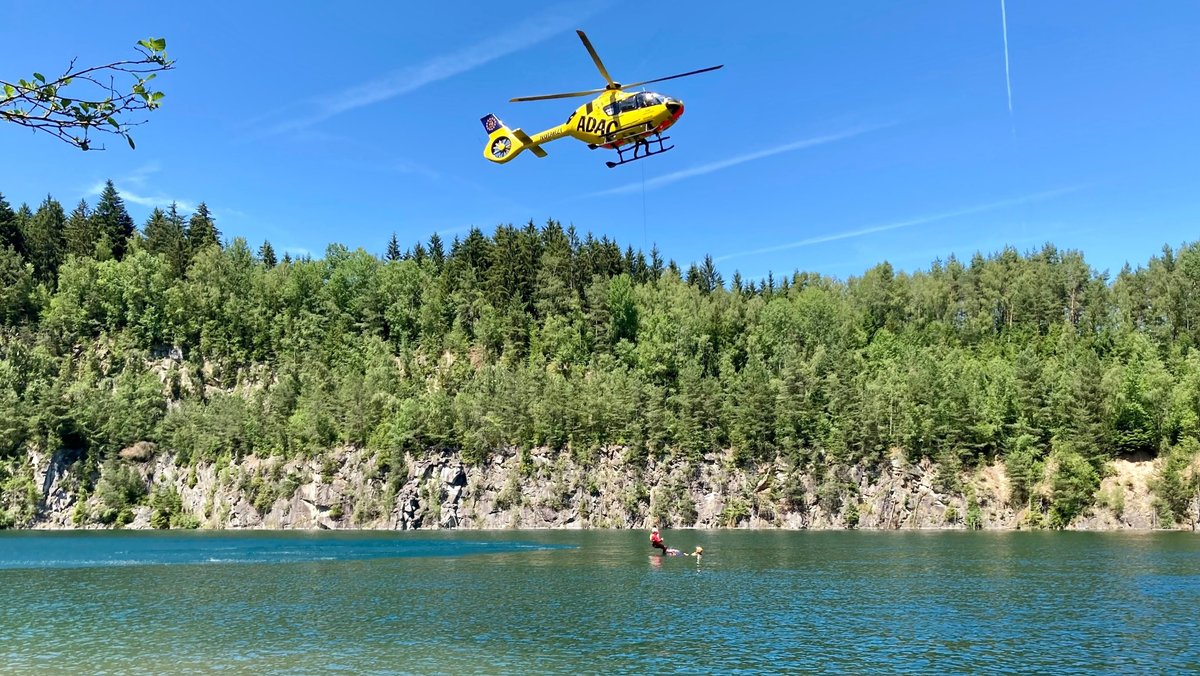 Ein ADAC-Hubschrauber schwebt über einem Gewässer und lässt per Seilwinde einen Notarzt hinunter.