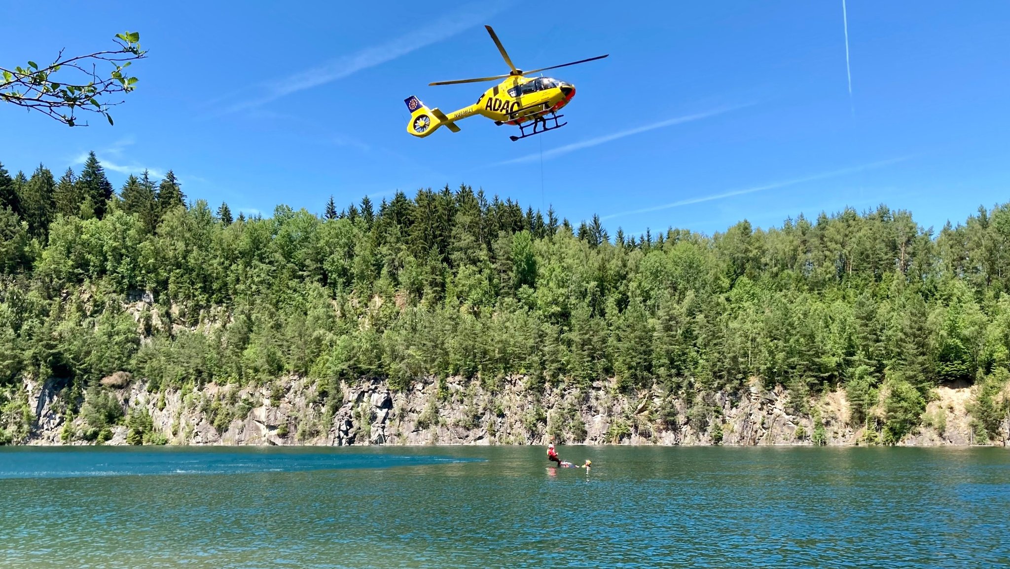 Ein ADAC-Hubschrauber schwebt über einem Gewässer und lässt per Seilwinde einen Notarzt hinunter. | Bild: BR/Renate Roßberger Ein ADAC-Hubschrauber schwebt über einem Gewässer und lässt per Seilwinde einen Notarzt hinunter.