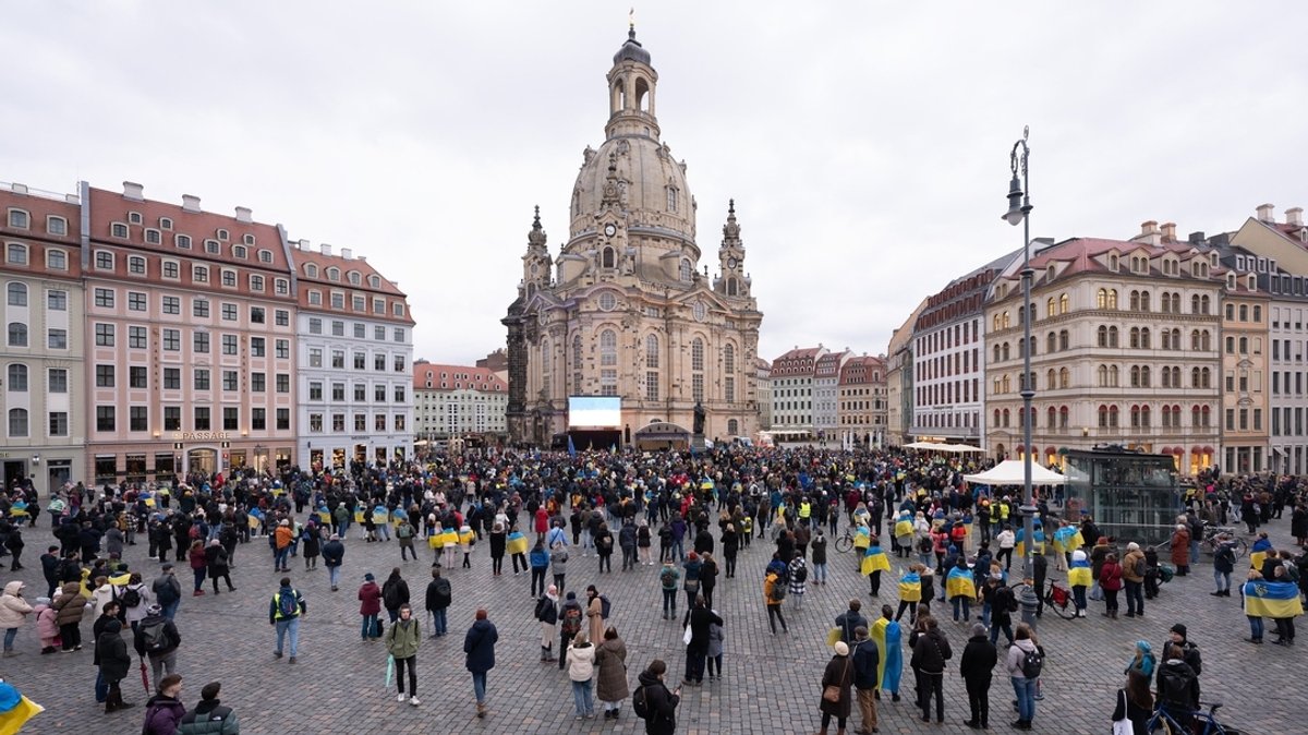 24.02.2023, Sachsen, Dresden: Teilnehmer einer Friedenskundgebung stehen auf dem Neumarkt vor der Frauenkirche. Die russische Armee hatte die Ukraine am 24.02.2022 überfallen.