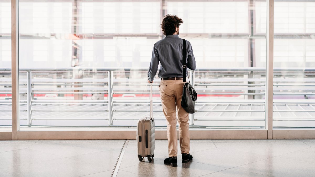 Ein Mann steht mit einem kleinen Reisekoffer am Flughafen.