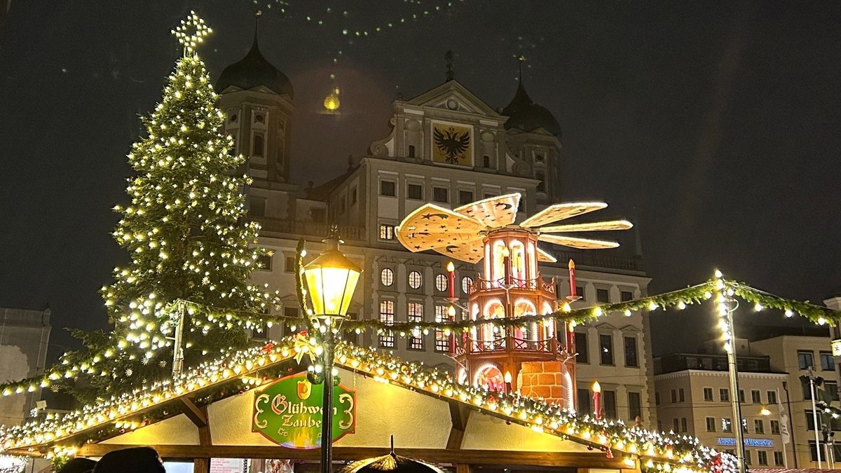Der diesjährige Augsburger Christkindlesmarkt ist eröffnet. Hell erleuchtet sind Baum und Buden.