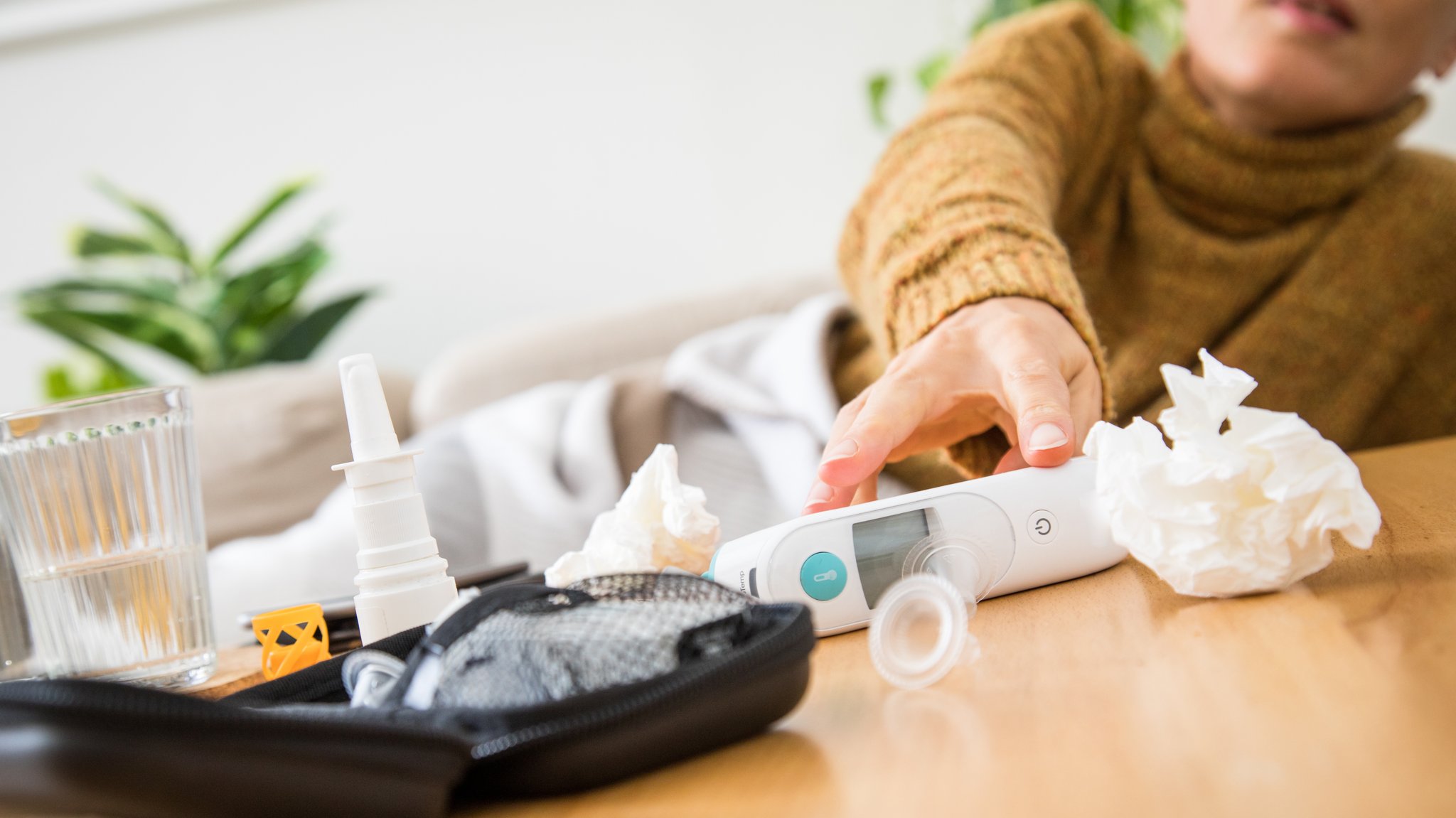 Frau liegt mit Taschentuch im Bett. Im Vordergrund Medikamente und Nasenspray.