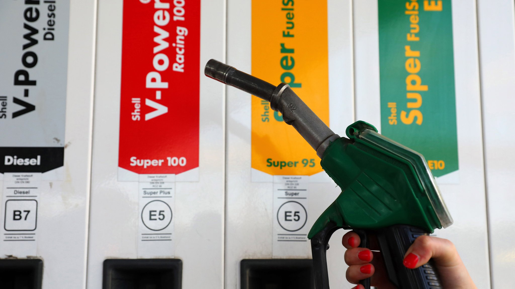 Ein Mensch hält die Zapfpistole an einer Tankstelle in der Hand. 