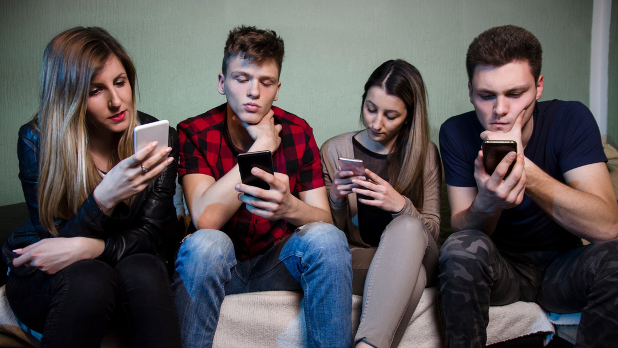 Vier junge Erwachsene schauen in ihre Smartphones.
