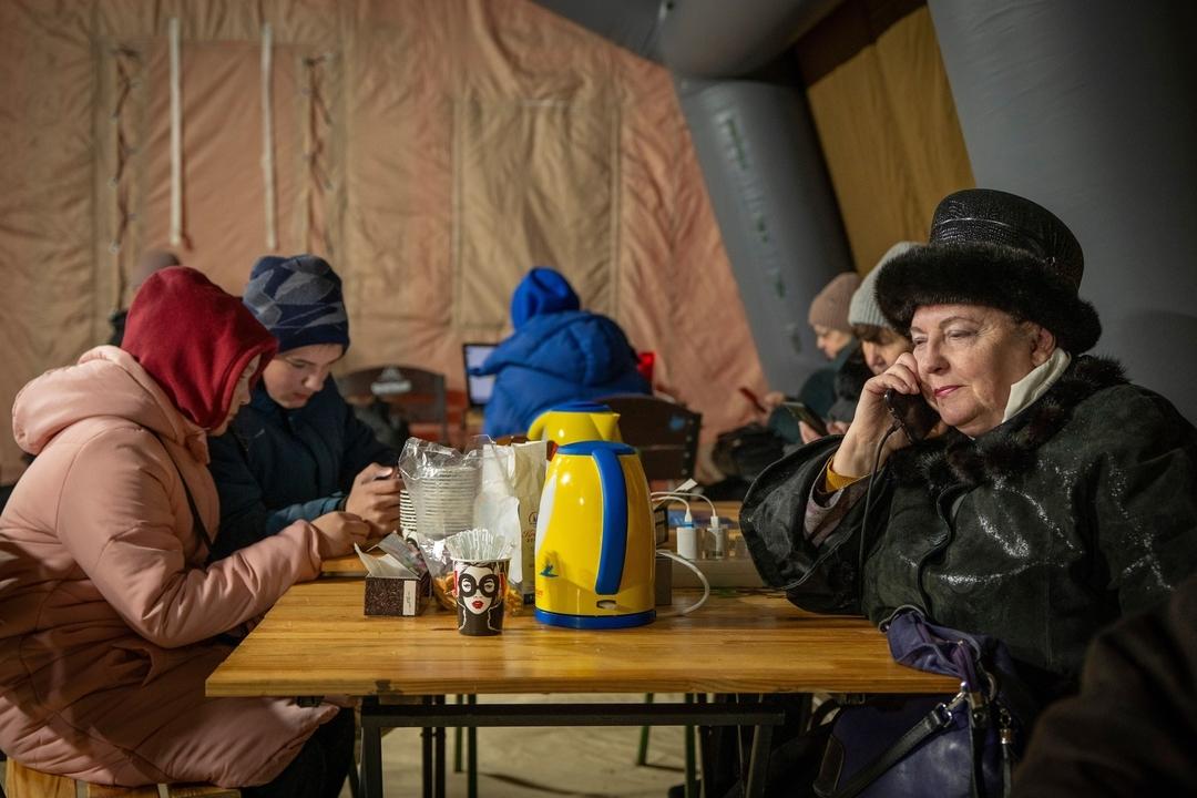 13.01.2026, Ukraine, Kiew: Menschen wärmen sich und laden ihre Akkus in einem Zelt auf, das der Rettungsdienst nach den russischen Luftangriffen auf den ukrainischen Energiesektor aufgestellt hat. Ein Teil der Bewohner der Stadt sind mitten im Winter ohne Strom, Wasser und Heizung. 