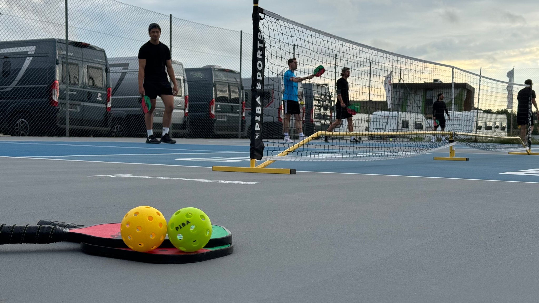 Zwei Pickleball-Schläger und -Bälle liegen auf einem Spielfeld. 